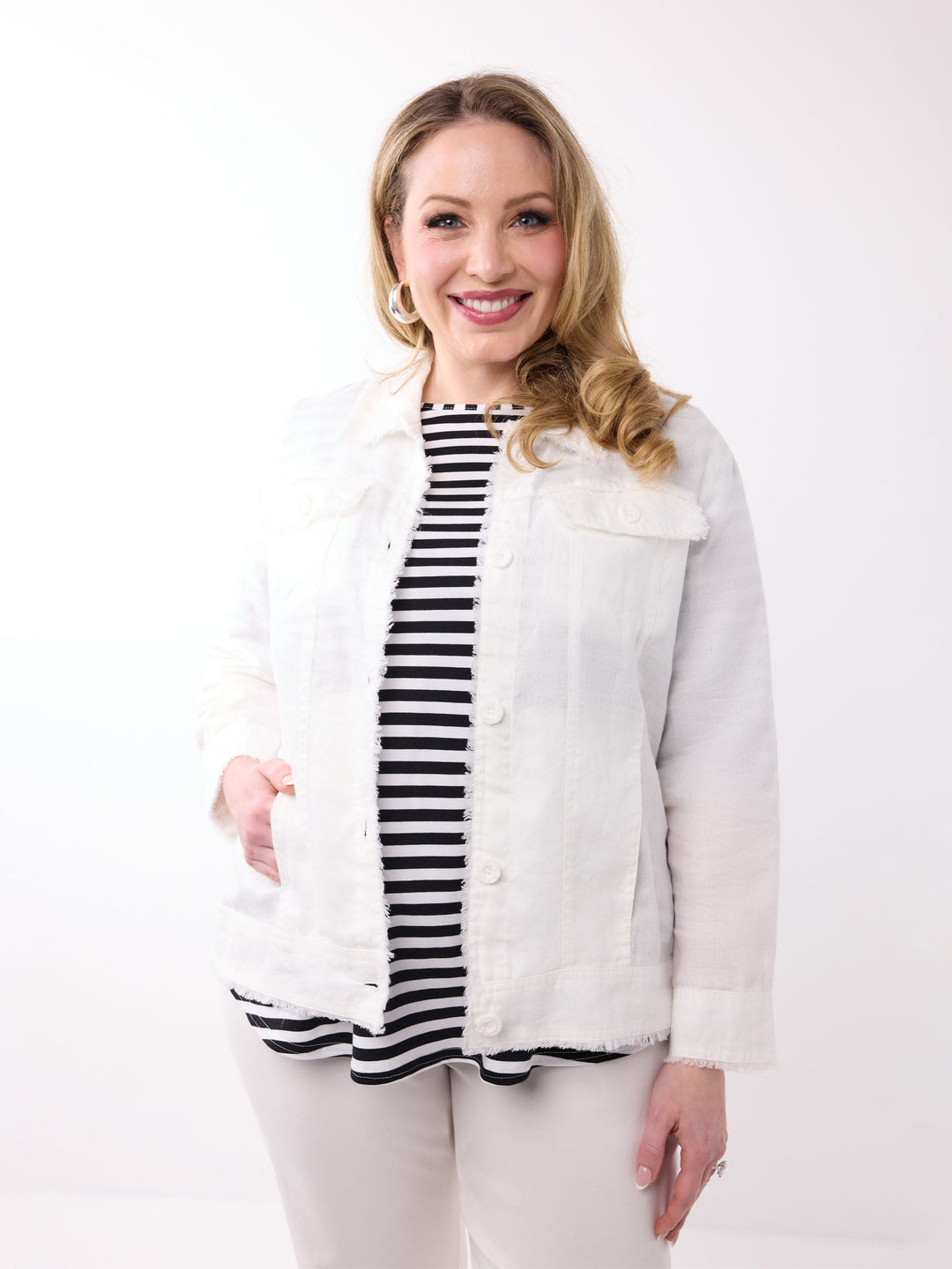 A woman wearing a white lightweight linen jacket over a black and white striped top, paired with white pants