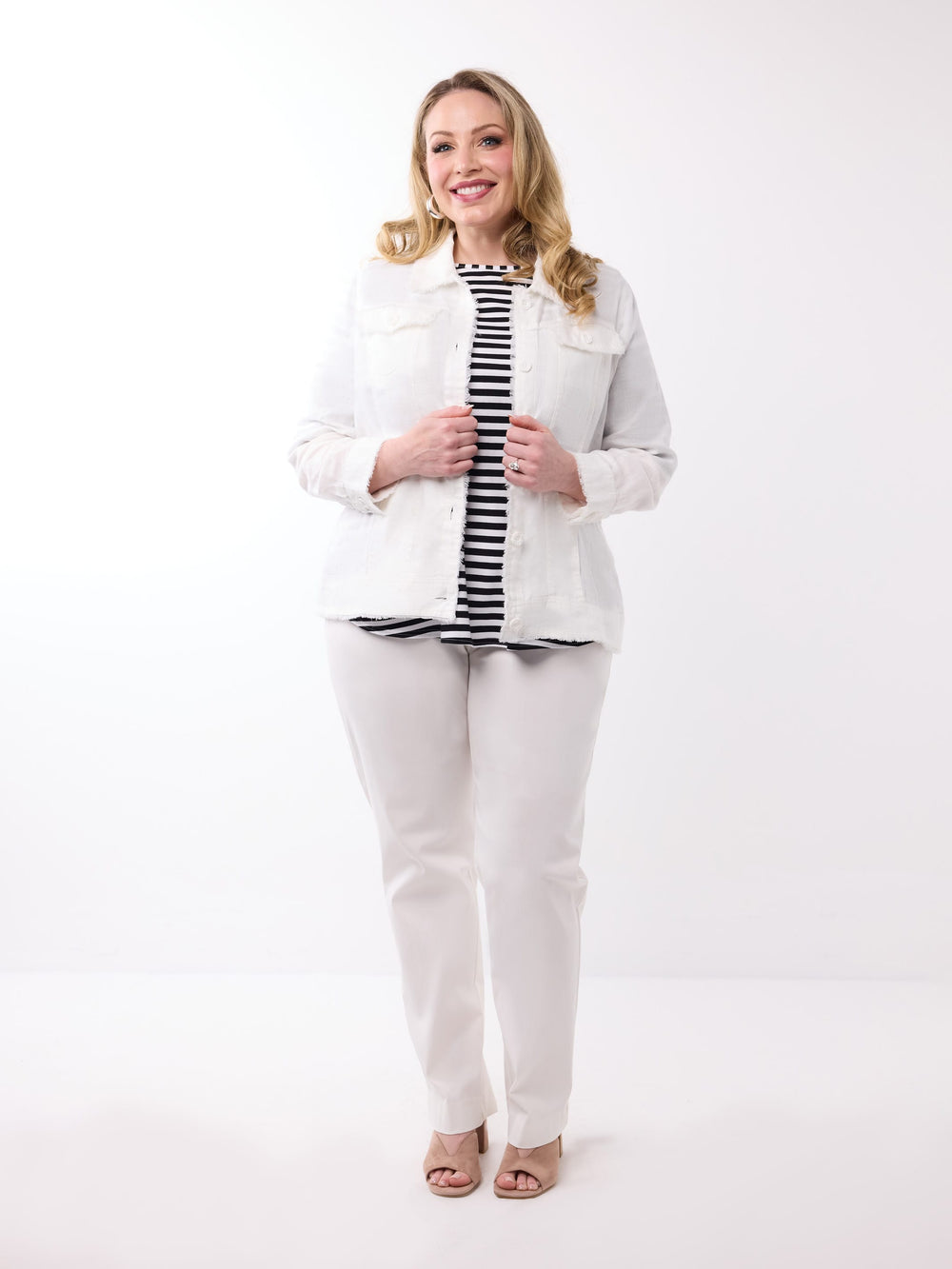 A woman wearing a white lightweight linen jacket over a black and white striped top, paired with white pants