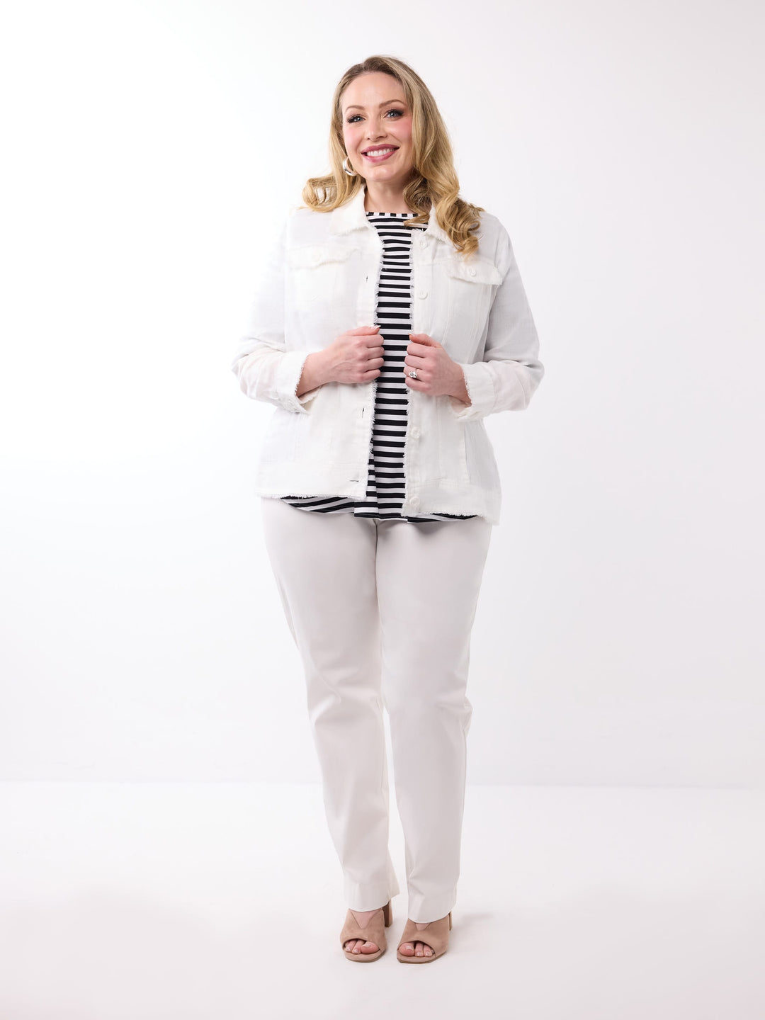 A woman wearing a white lightweight linen jacket over a black and white striped top, paired with white pants