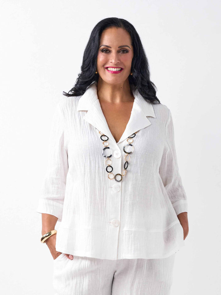 A woman wearing a white textured linen and cotton blend three-quarter sleeve blazer and matching white pants