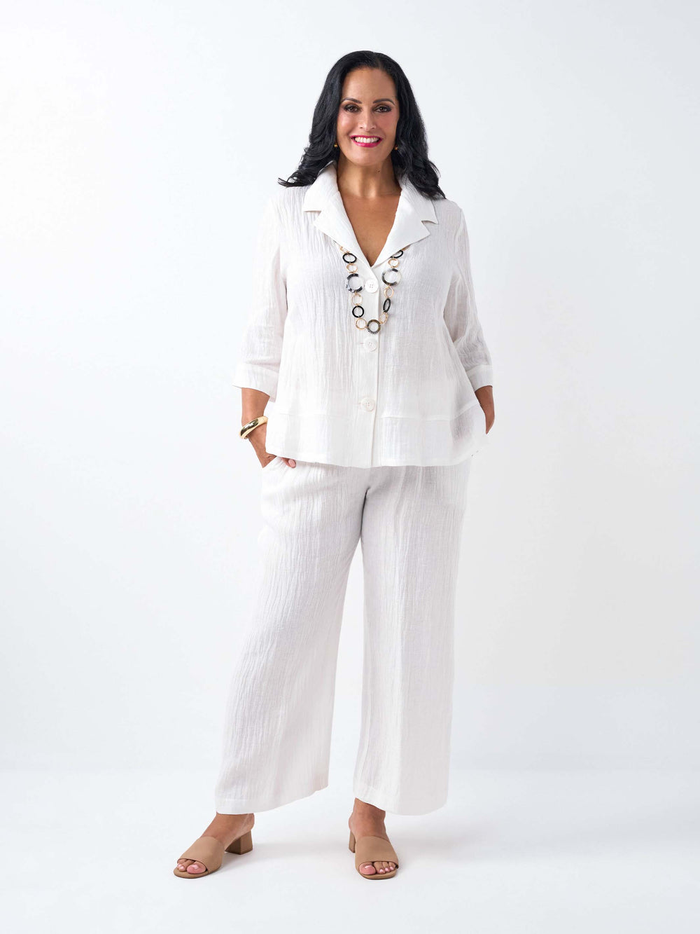 A woman wearing a white textured linen and cotton blend three-quarter sleeve blazer and matching white pants