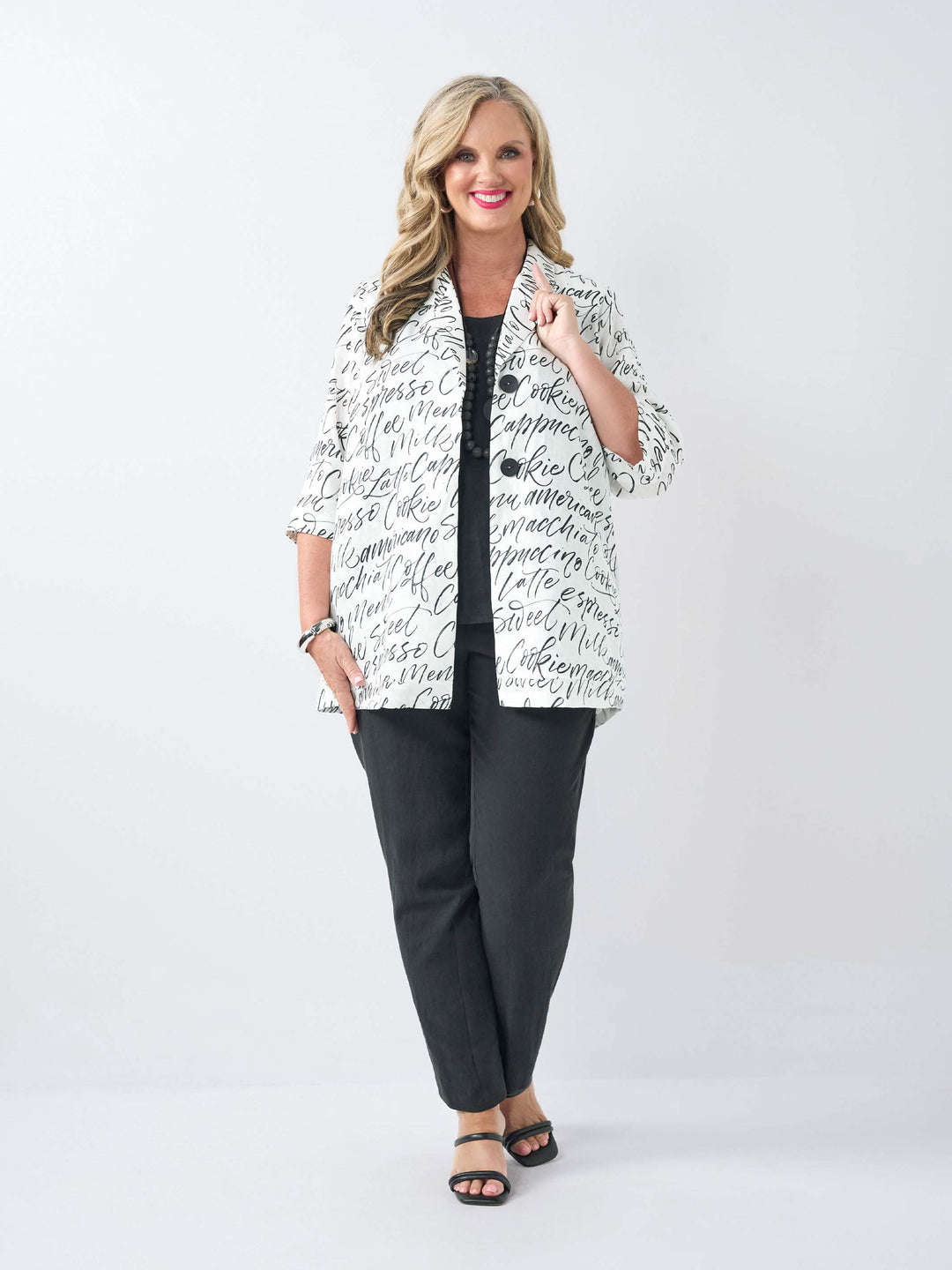 A woman wearing a white short-sleeve button-front jacket covered in black cursive script text, over a black top and black pants.