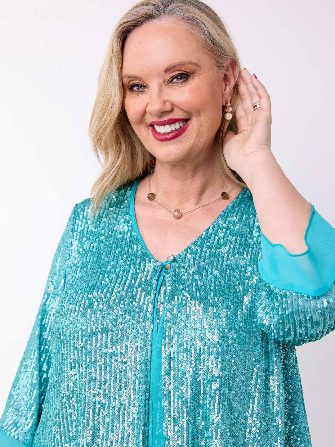 A woman wearing a sparkling teal sequined evening jacket with sheer elbow-length sleeves and a V-neckline