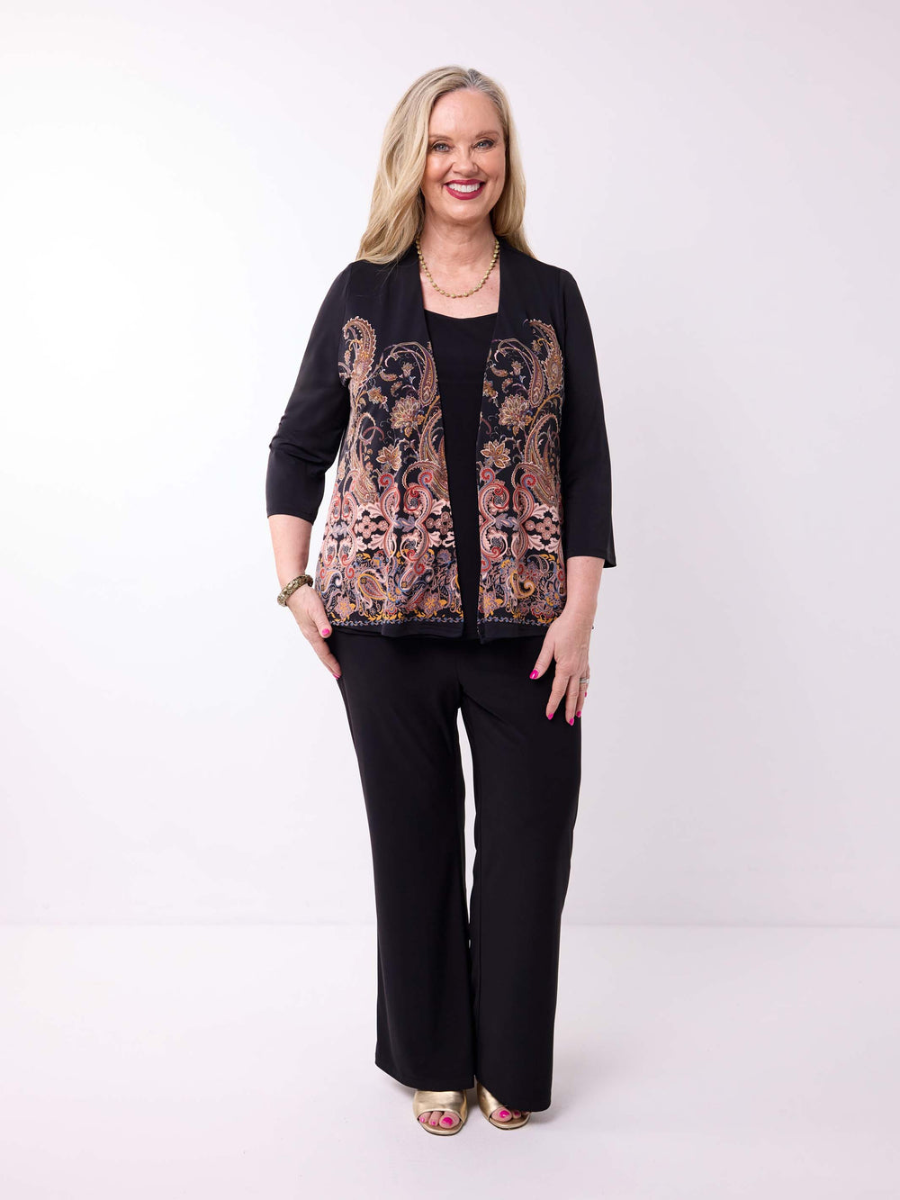 A woman modeling a black three-quarter sleeve jacket with a colourful paisley pattern on the front, paired with black wide-leg pants
