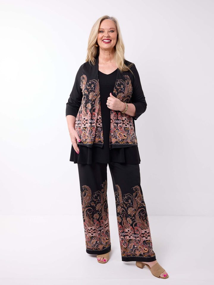 A woman wearing a black three-quarter sleeve short jacket with a large paisley pattern panel in black, gold, and rust. Paired with matching palazzo pant