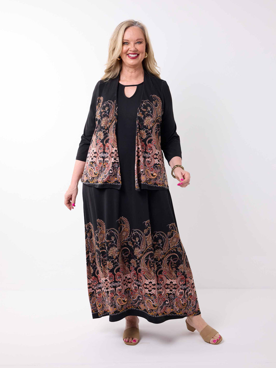 A woman wearing a black three-quarter sleeve short jacket with a large paisley pattern panel in black, gold, and rust. Paired with a matching maxi dress