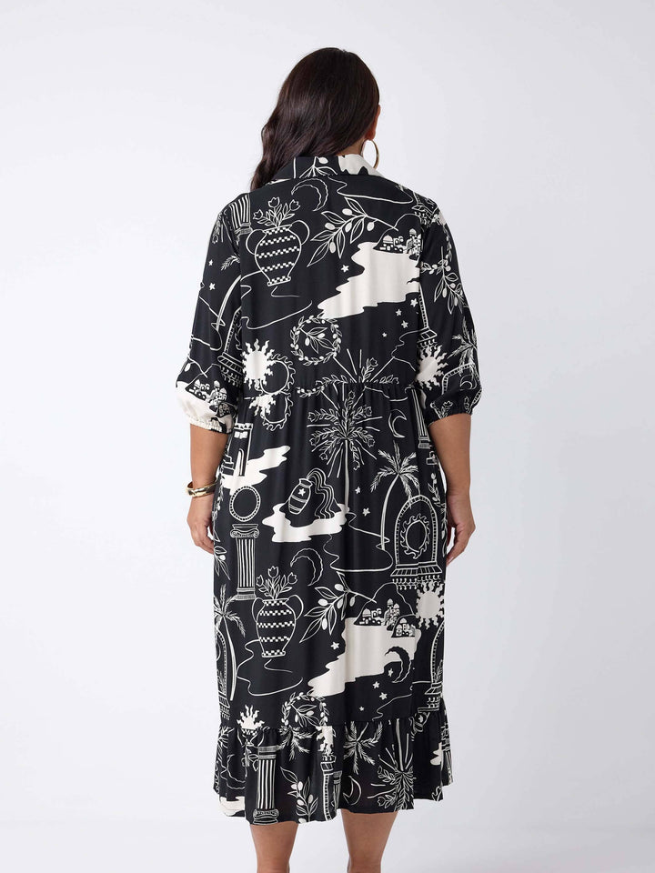 A woman viewed from the back wearing a black midi dress with a white botanical and architectural line print