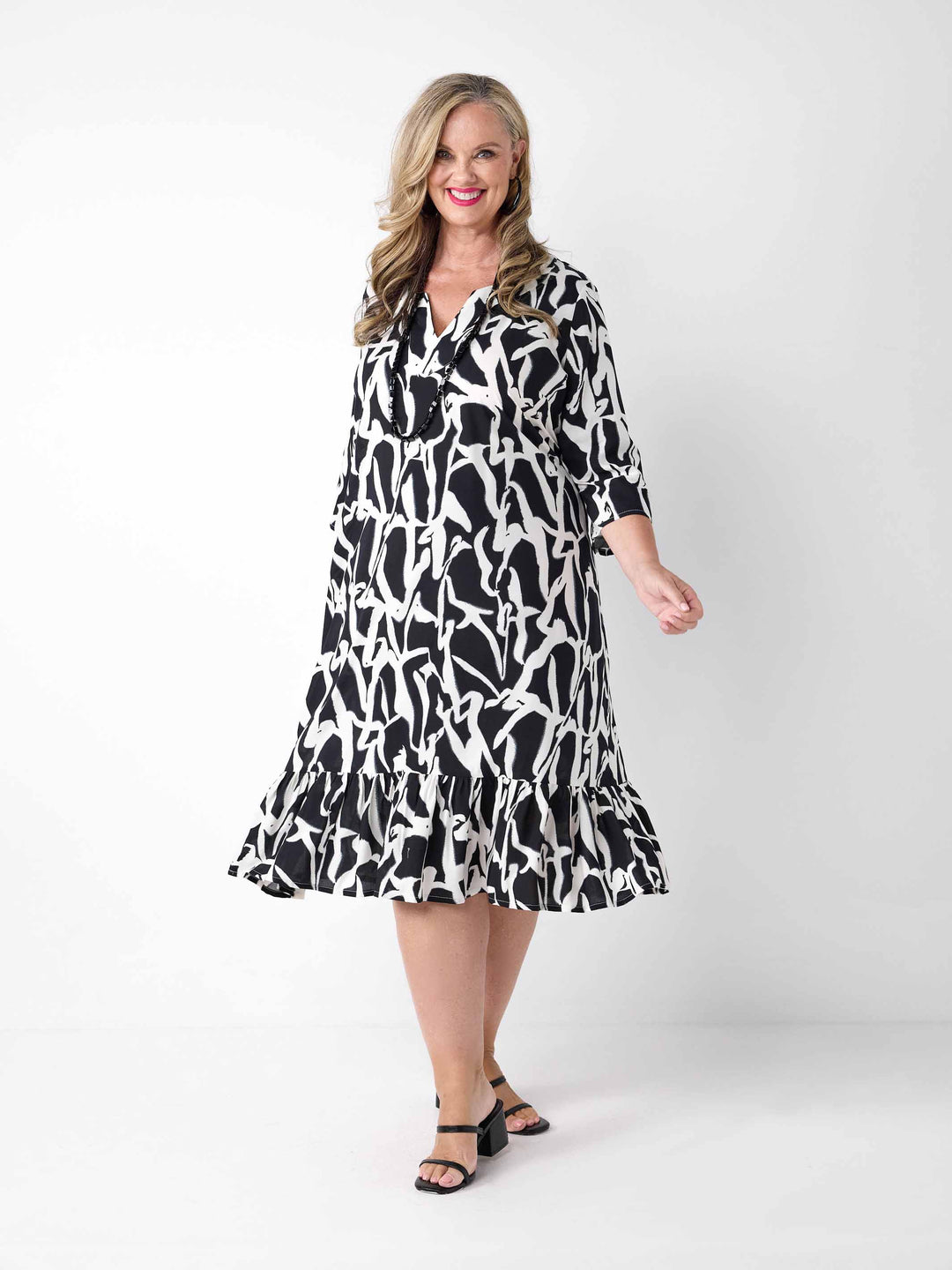 A woman wearing a black and white abstract patterned midi dress with three-quarter sleeves and a ruffled hem