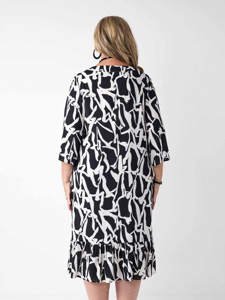 A woman wearing a black and white abstract patterned midi dress with three-quarter sleeves and a ruffled hem