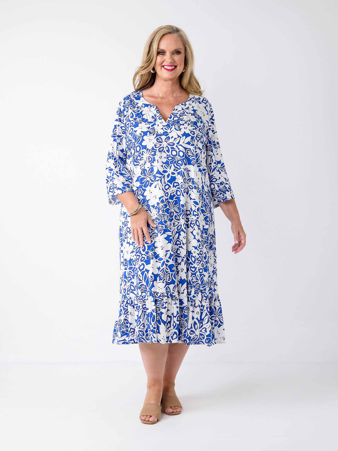 A woman wearing a blue and white floral print midi dress with three-quarter sleeves, frill hemline, and a V-inset-neckline