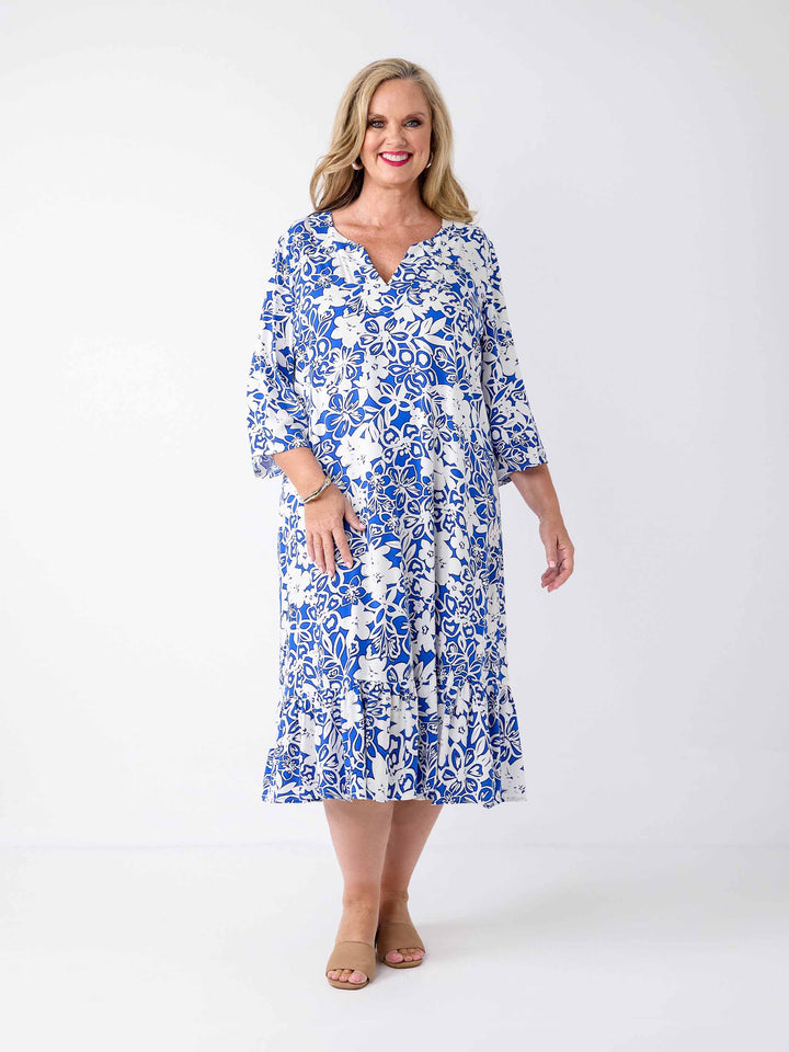 A woman wearing a blue and white floral print midi dress with three-quarter sleeves, frill hemline, and a V-inset-neckline