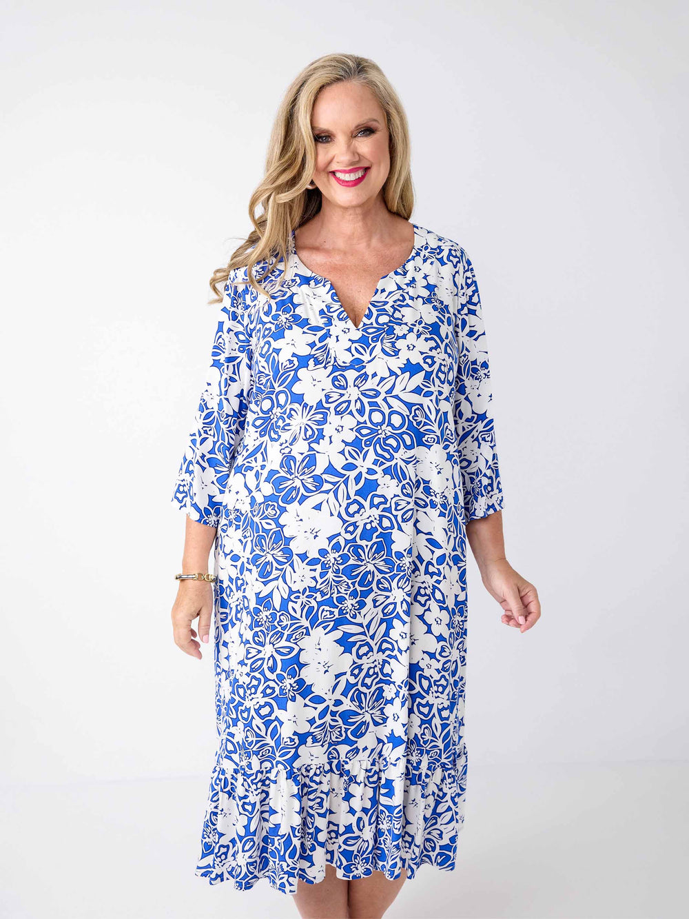 A woman wearing a blue and white floral print midi dress with three-quarter sleeves, frill hemline, and a V-inset-neckline