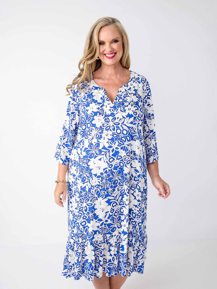 A woman wearing a blue and white floral print midi dress with three-quarter sleeves, frill hemline, and a V-inset-neckline
