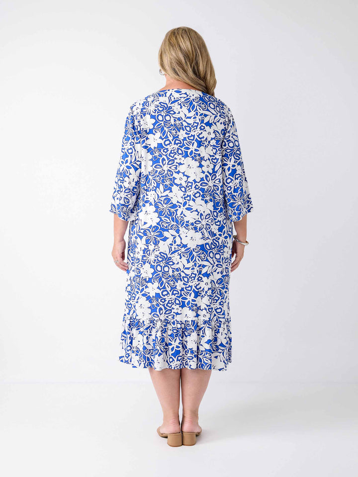 A woman wearing a blue and white floral print midi dress with three-quarter sleeves, frill hemline, and a V-inset-neckline