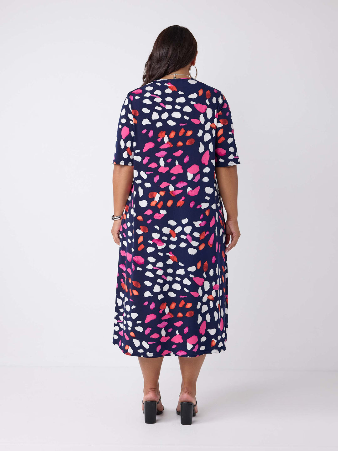 back view of model wearing a navy blue v-neck midi dress with colourful pebbles print of white and pink