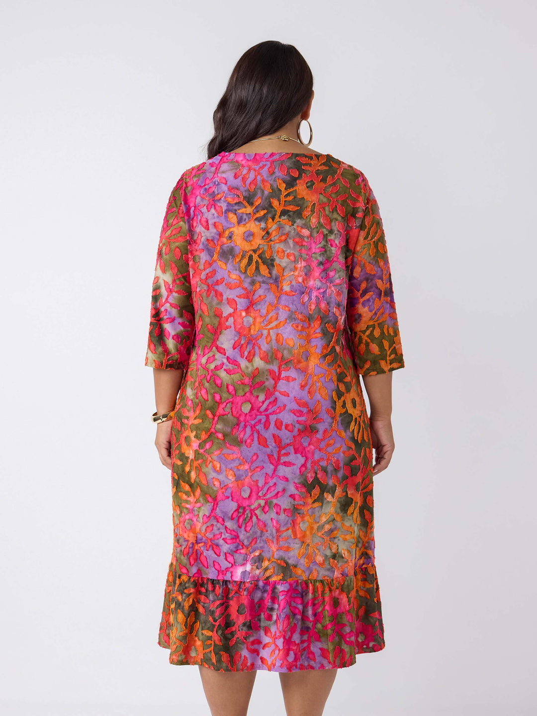 A woman viewed from the back wearing a colourful floral burnout print dress with three-quarter sleeves and a ruffled hem