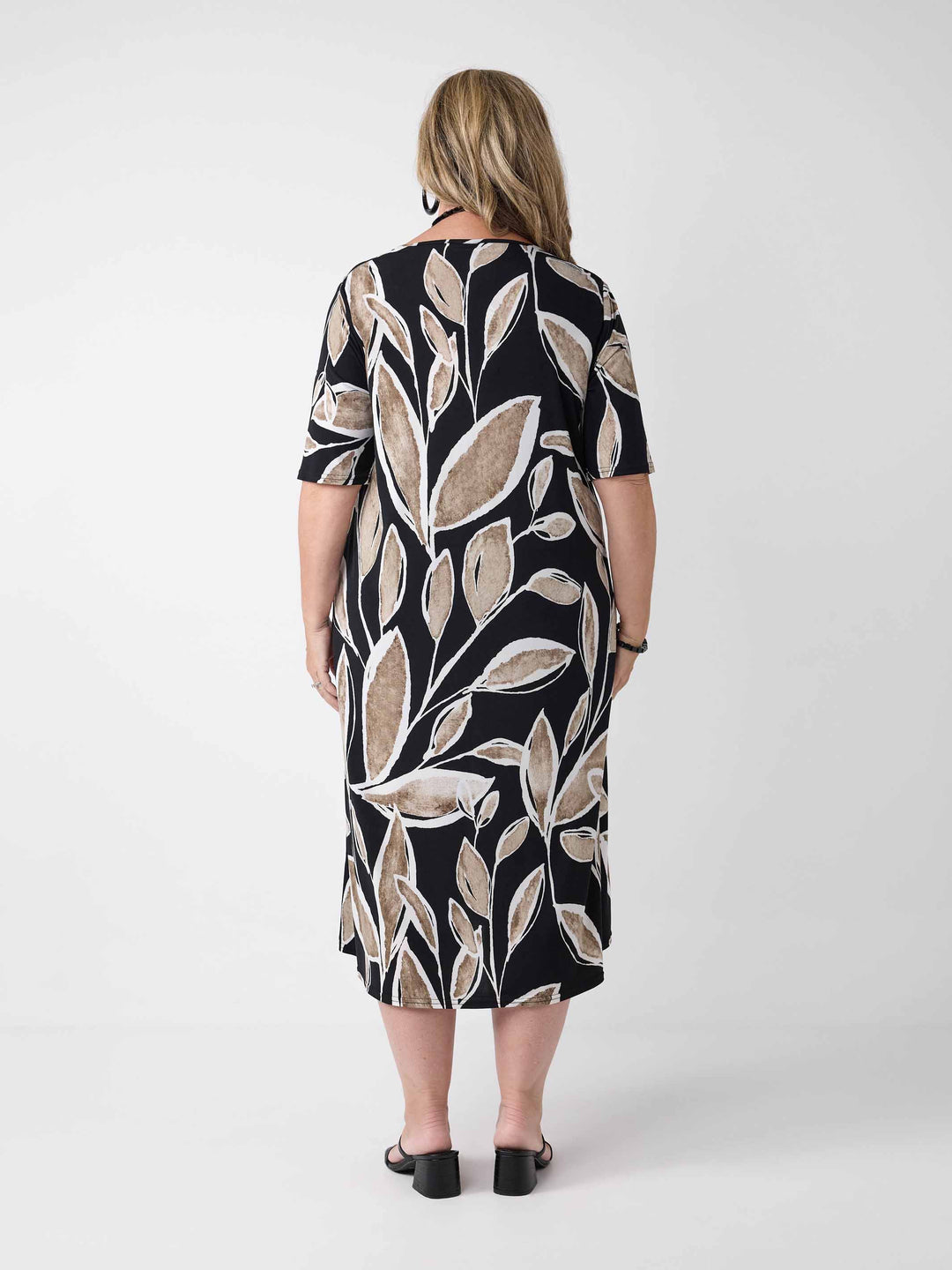 back view of model wearing a short-sleeve midi dress with a black background and a beige leaf pattern