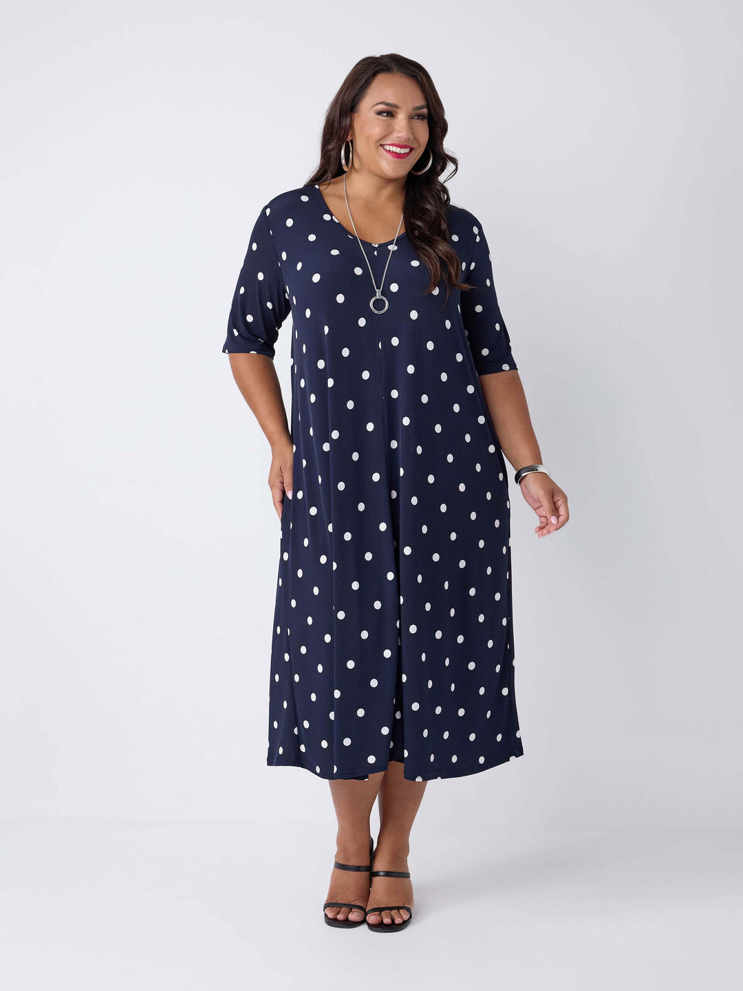 model wearing a navy blue midi dress with a white polka dot pattern, featuring short sleeves and a V-neckline