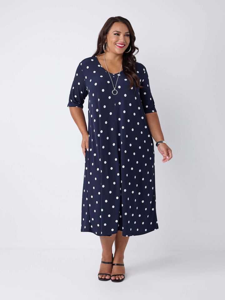 model wearing a navy blue midi dress with a white polka dot pattern, featuring short sleeves and a V-neckline