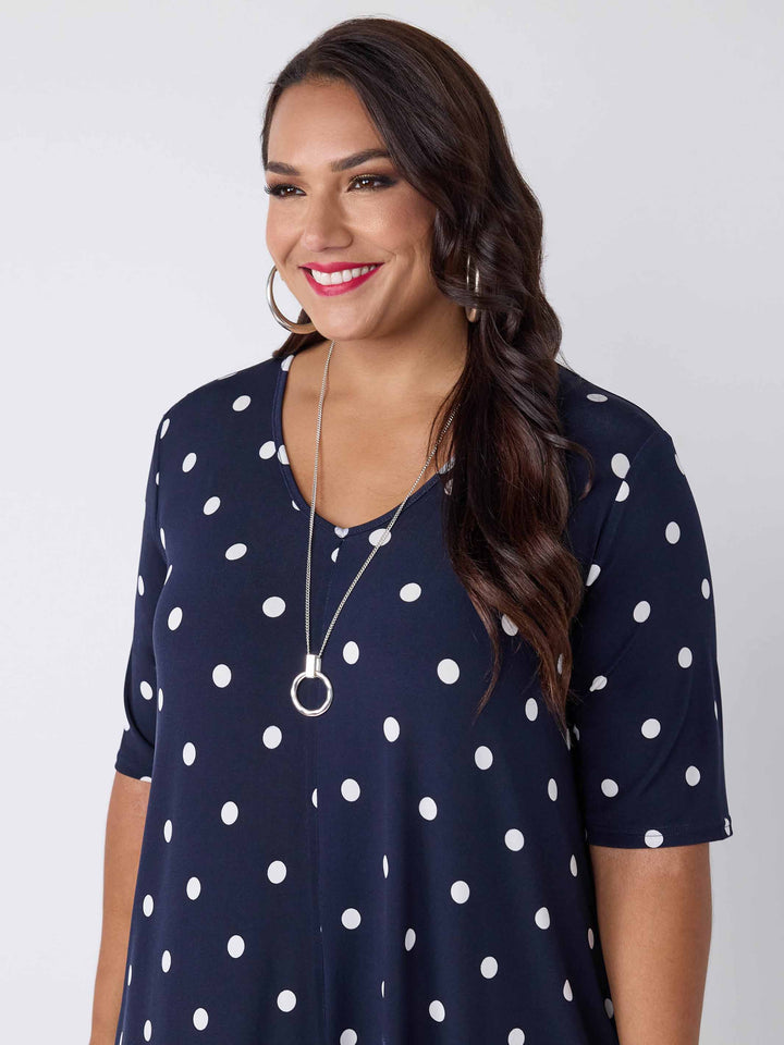 detail view of model wearing a navy blue midi dress with a white polka dot pattern, featuring short sleeves and a V-neckline