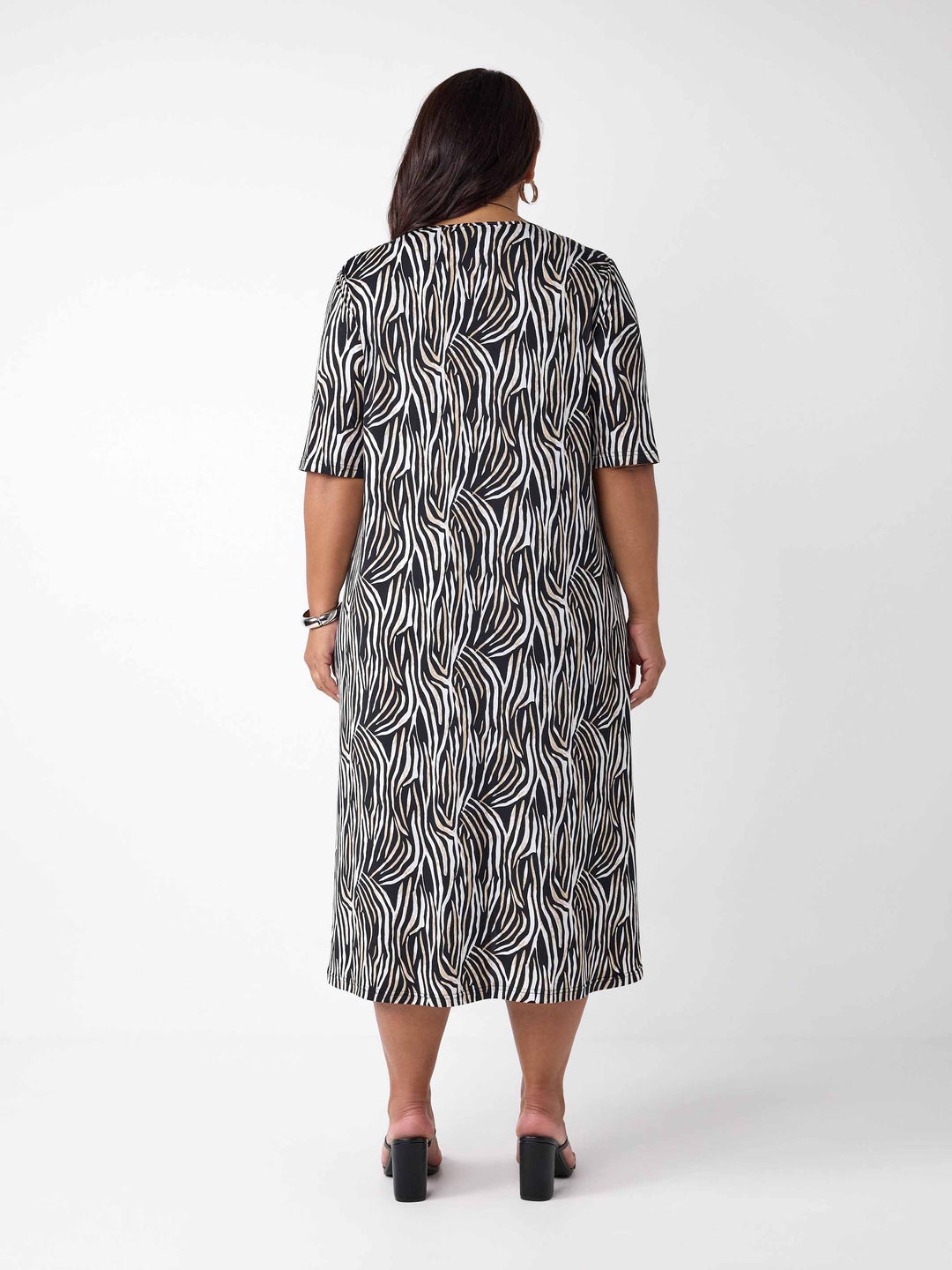 back view of model wearing a black, white, and brown zebra-print midi dress with three-quarter sleeves and side pockets