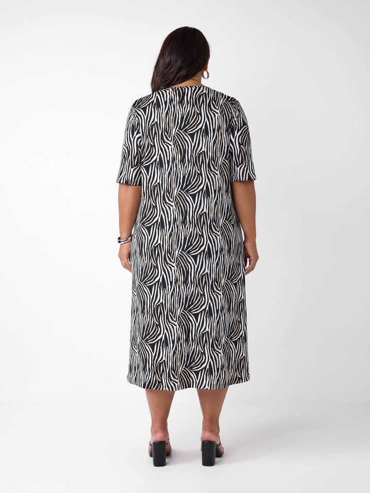 back view of model wearing a black, white, and brown zebra-print midi dress with three-quarter sleeves and side pockets