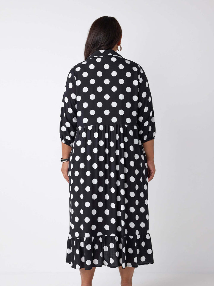 A woman viewed from the back wearing a black midi dress with a white polka dot pattern