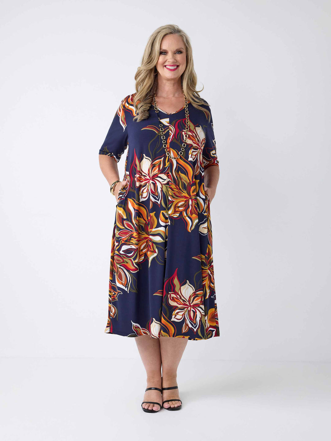 model wearing a short-sleeve midi dress with a navy blue base and a vibrant orange, red, and white floral print