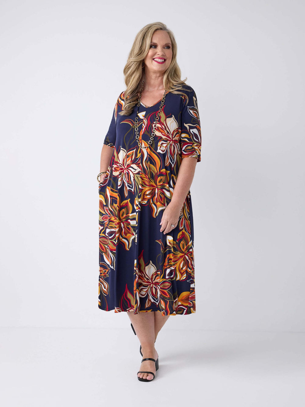 model wearing a short-sleeve midi dress with a navy blue base and a vibrant orange, red, and white floral print