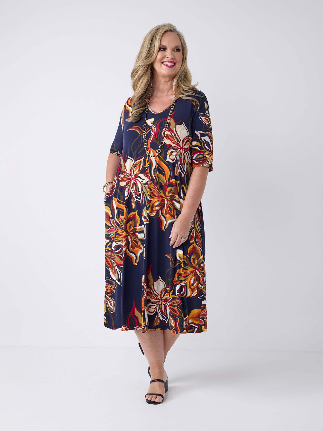 model wearing a short-sleeve midi dress with a navy blue base and a vibrant orange, red, and white floral print