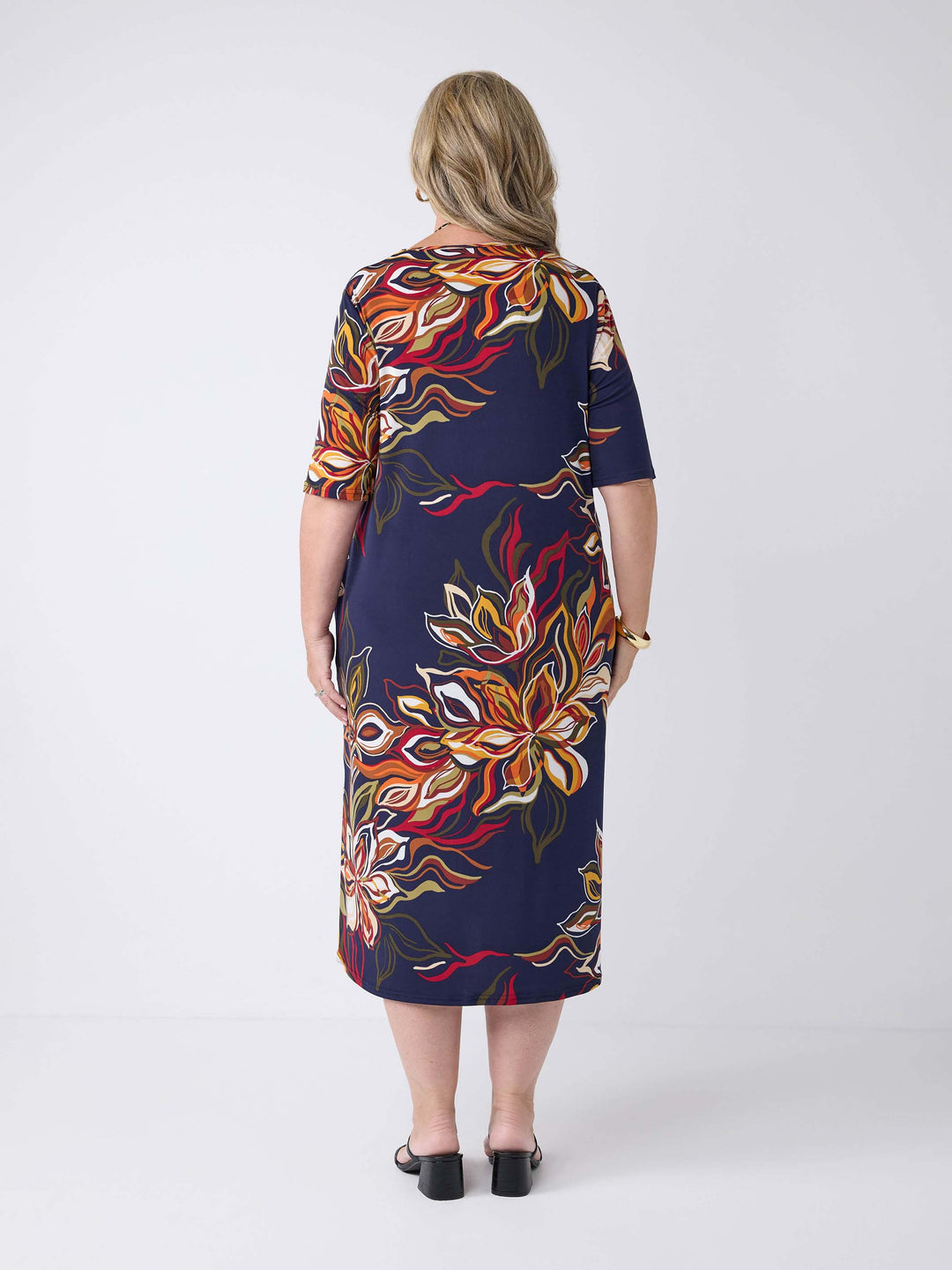 back view of model wearing a short-sleeve midi dress with a navy blue base and a vibrant orange, red, and white floral print