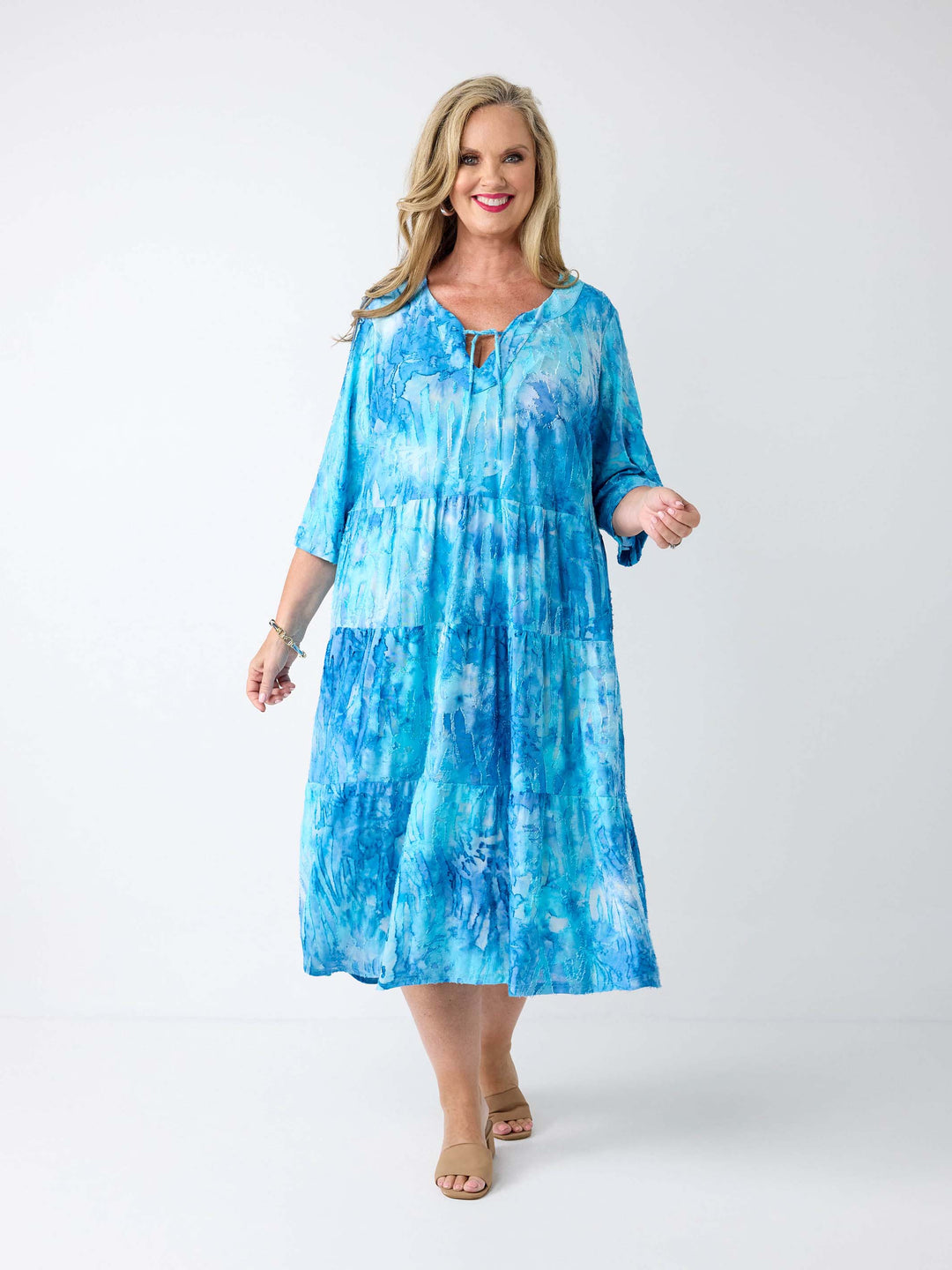A woman wearing a aqua blue tie die tiered midi dress with tie front v-neckline