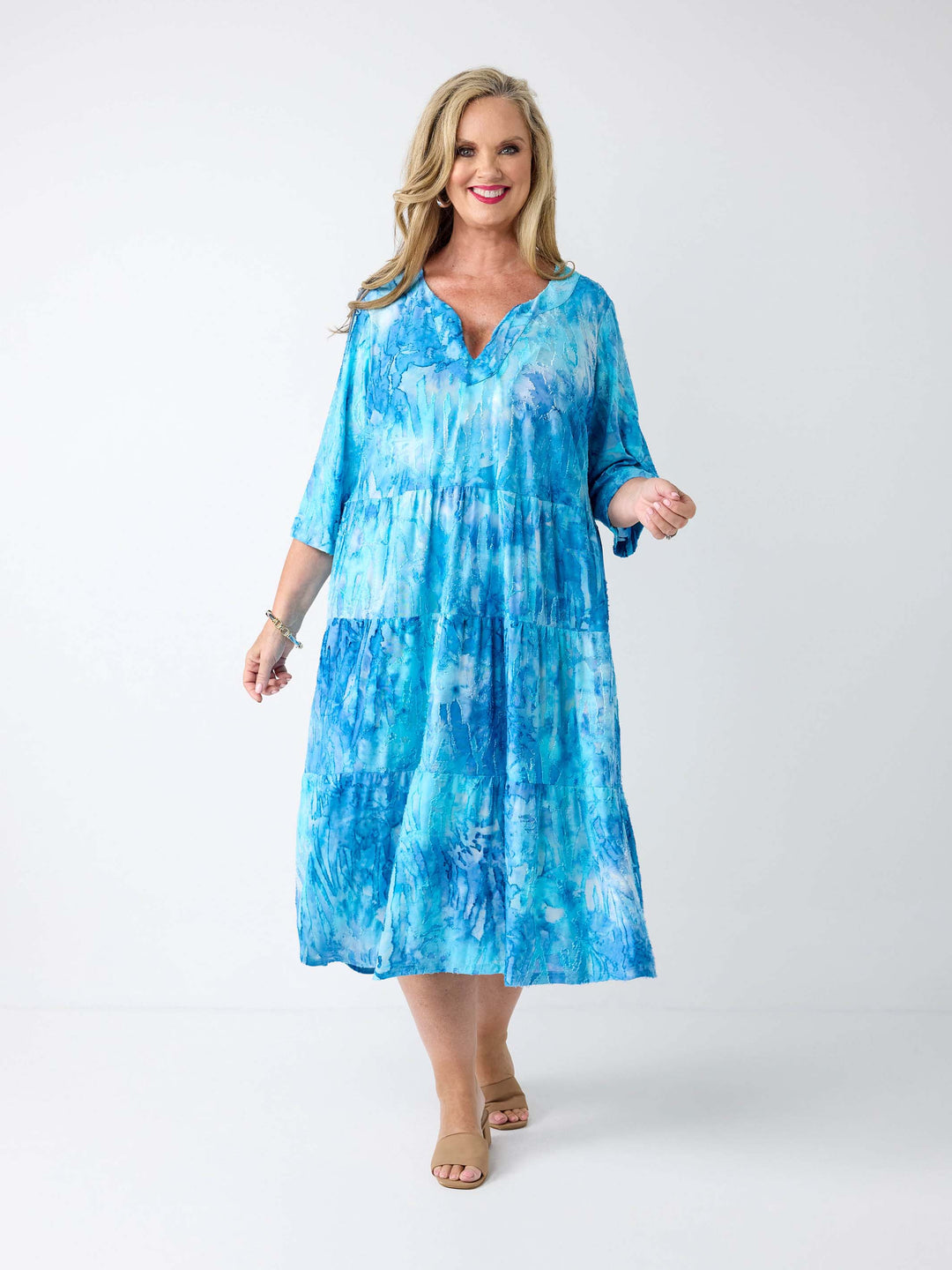 A woman wearing a aqua blue tie die tiered midi dress with tie front v-neckline