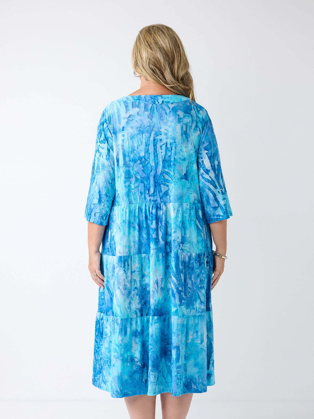 A woman wearing a aqua blue tie die tiered midi dress with tie front v-neckline