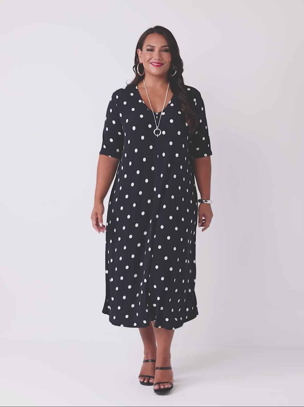 video of model wearing a navy blue midi dress with a white polka dot pattern, featuring short sleeves and a V-neckline