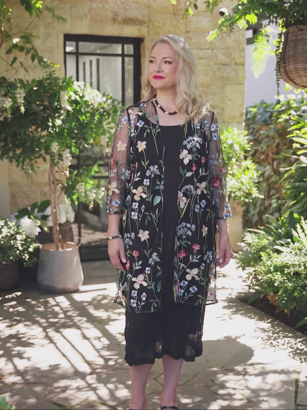 video of a woman wearing a sheer black embroidered evening jacket over a black crushed dress