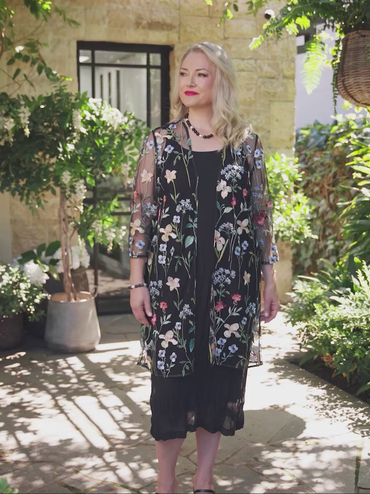 video of a woman wearing a sheer black embroidered evening jacket over a black crushed dress