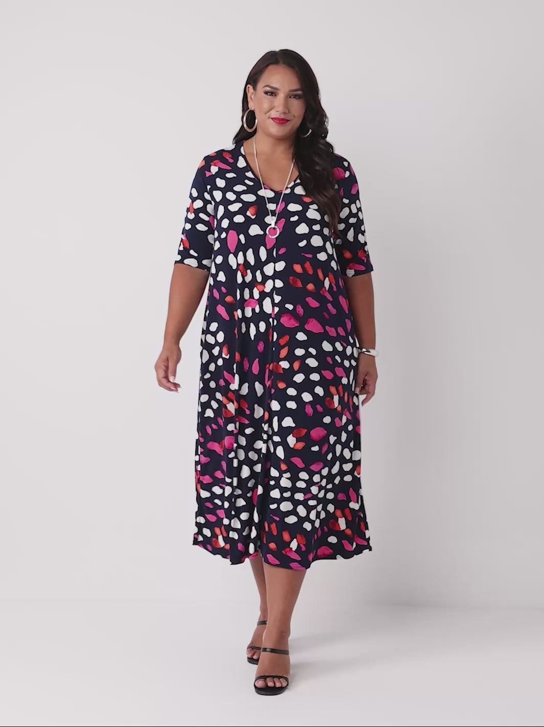 video of model wearing a navy blue v-neck midi dress with colourful pebbles print of white and pink