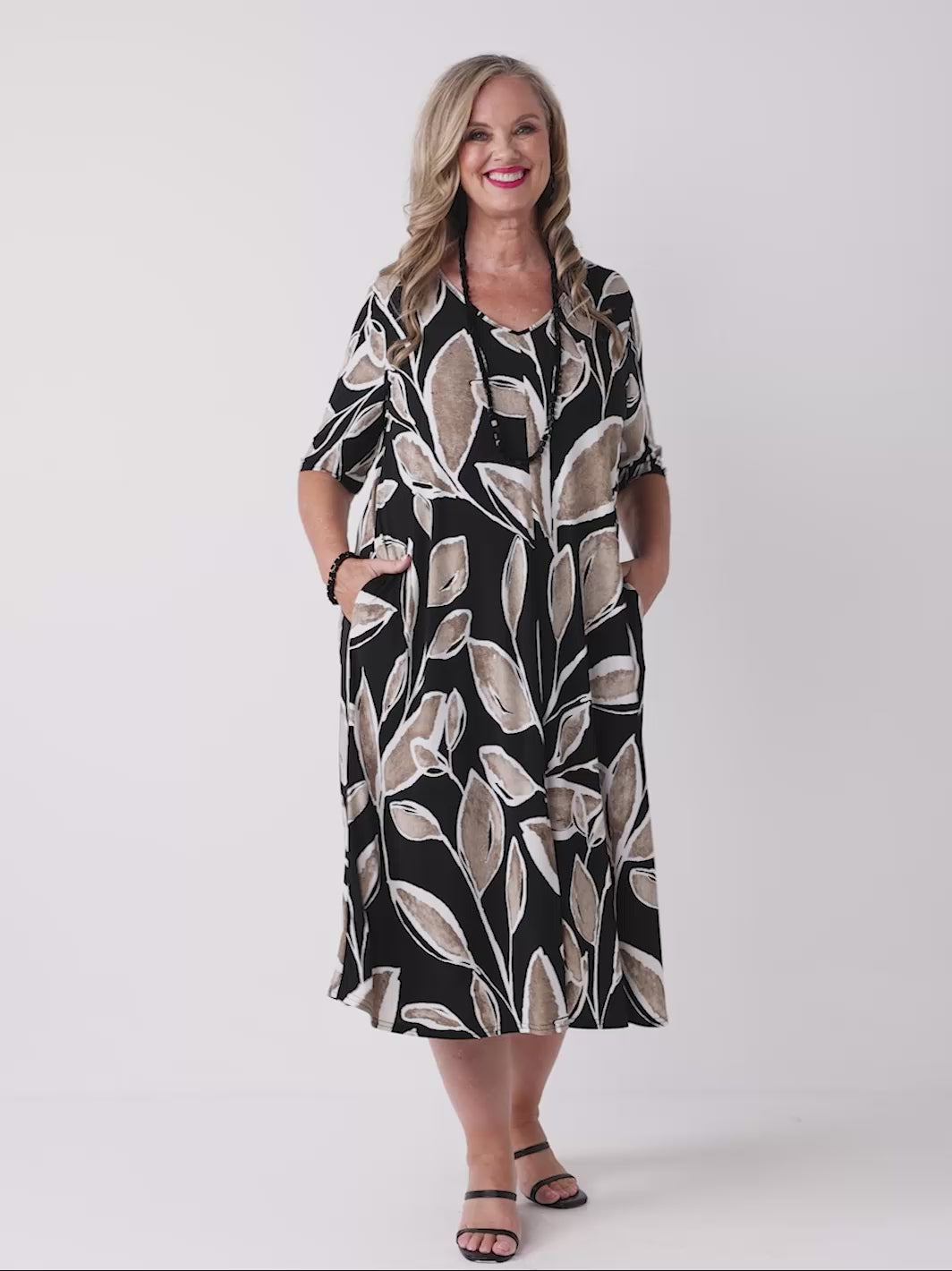 video of model wearing a short-sleeve midi dress with a black background and a beige leaf pattern