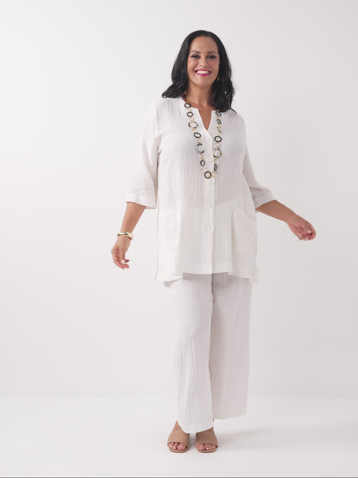 video of model wearing a white textured crinkle linen button-up top with two front pockets, paired with white crinkle linen pant