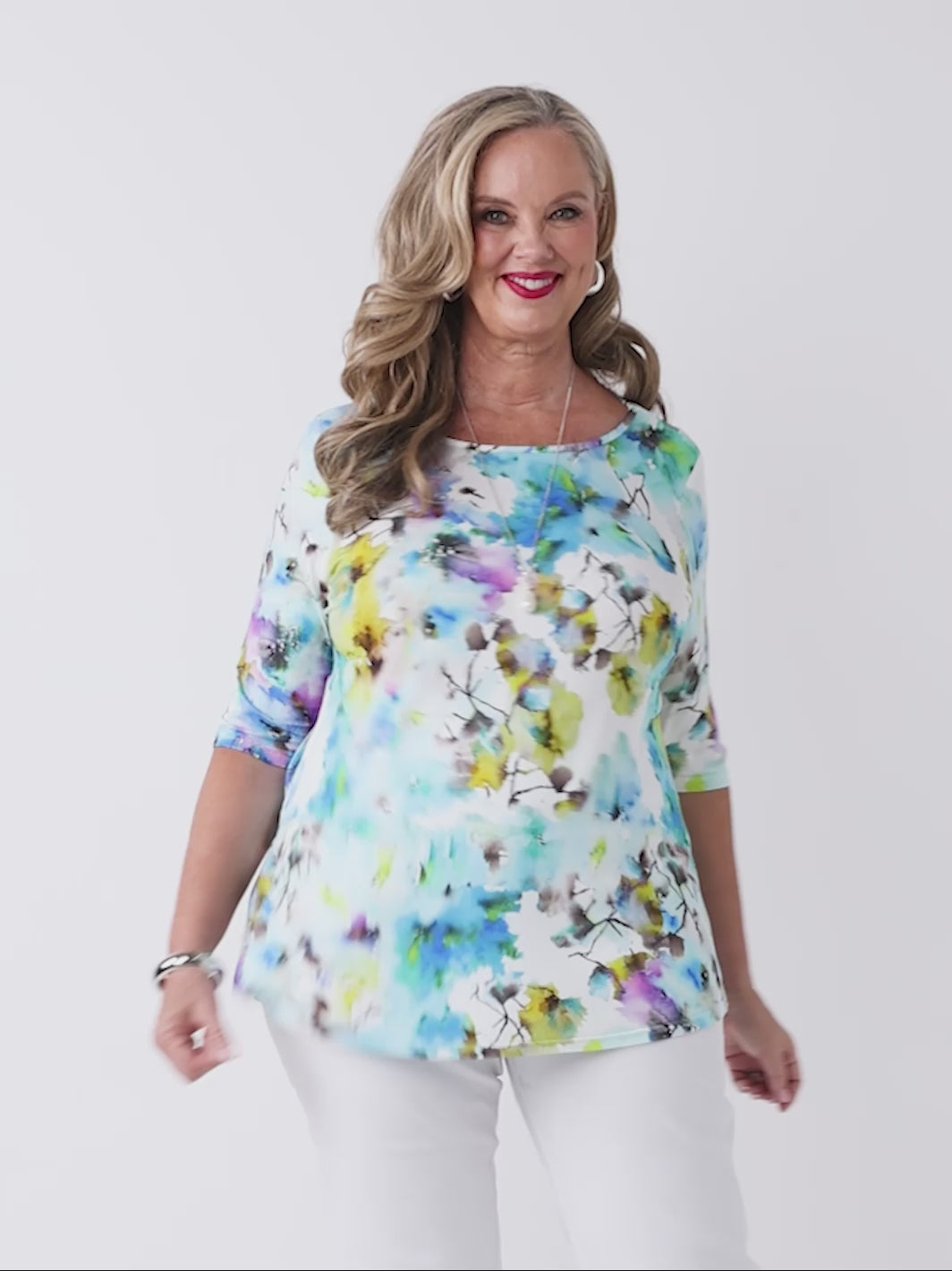 video of a woman wearing a colourful watercolour floral print top in blue with three-quarter sleeves and white pants