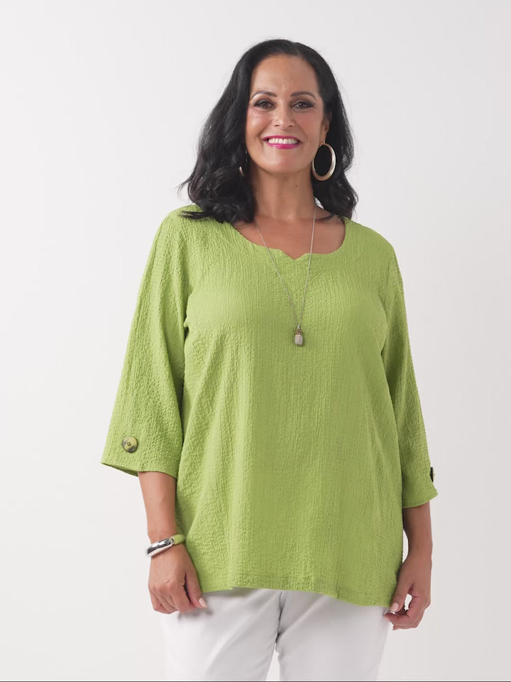 video of model wearing a lime green textured three-quarter sleeve top with decorative buttons on the cuffs