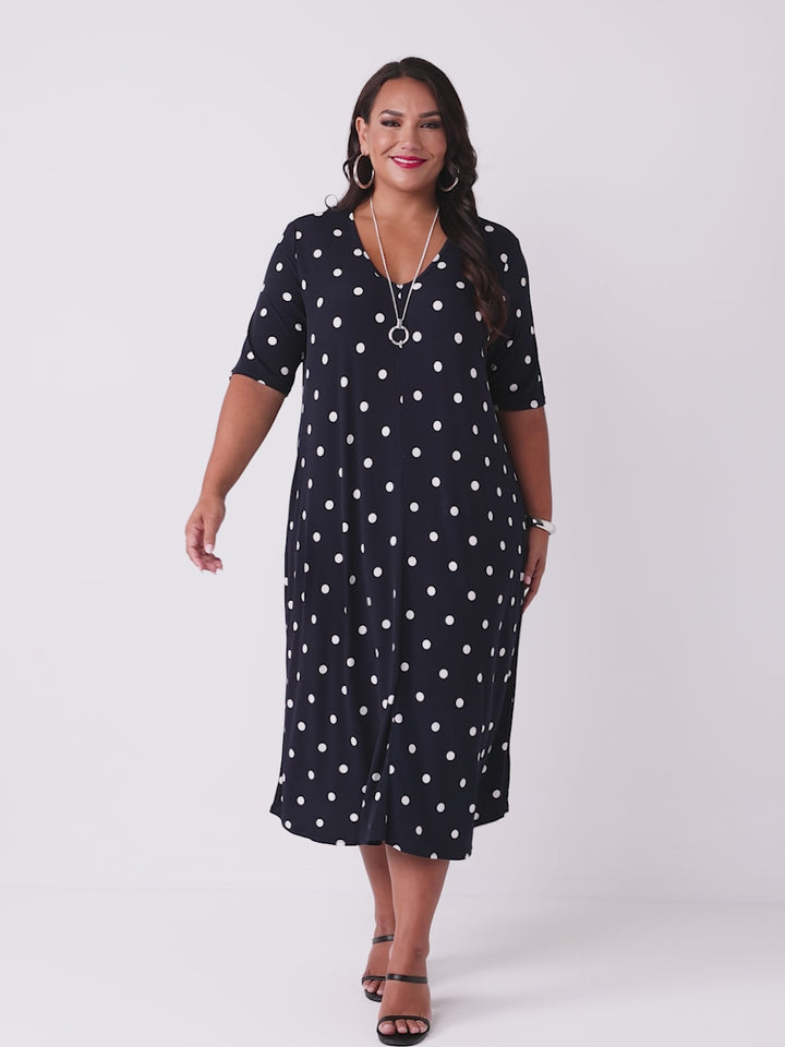 video of model wearing a navy blue midi dress with a white polka dot pattern, featuring short sleeves and a V-neckline