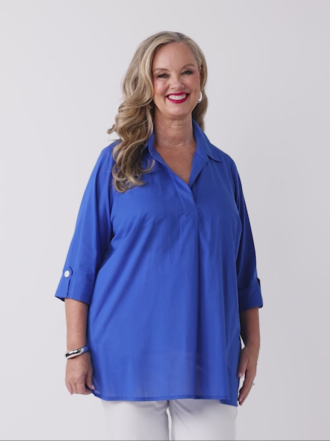 video of model wearing a bright royal blue collared cotton top with three-quarter tab sleeves and white pants