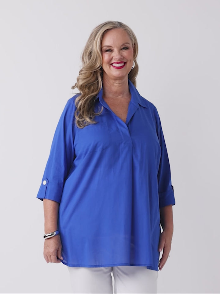 video of model wearing a bright royal blue collared cotton top with three-quarter tab sleeves and white pants
