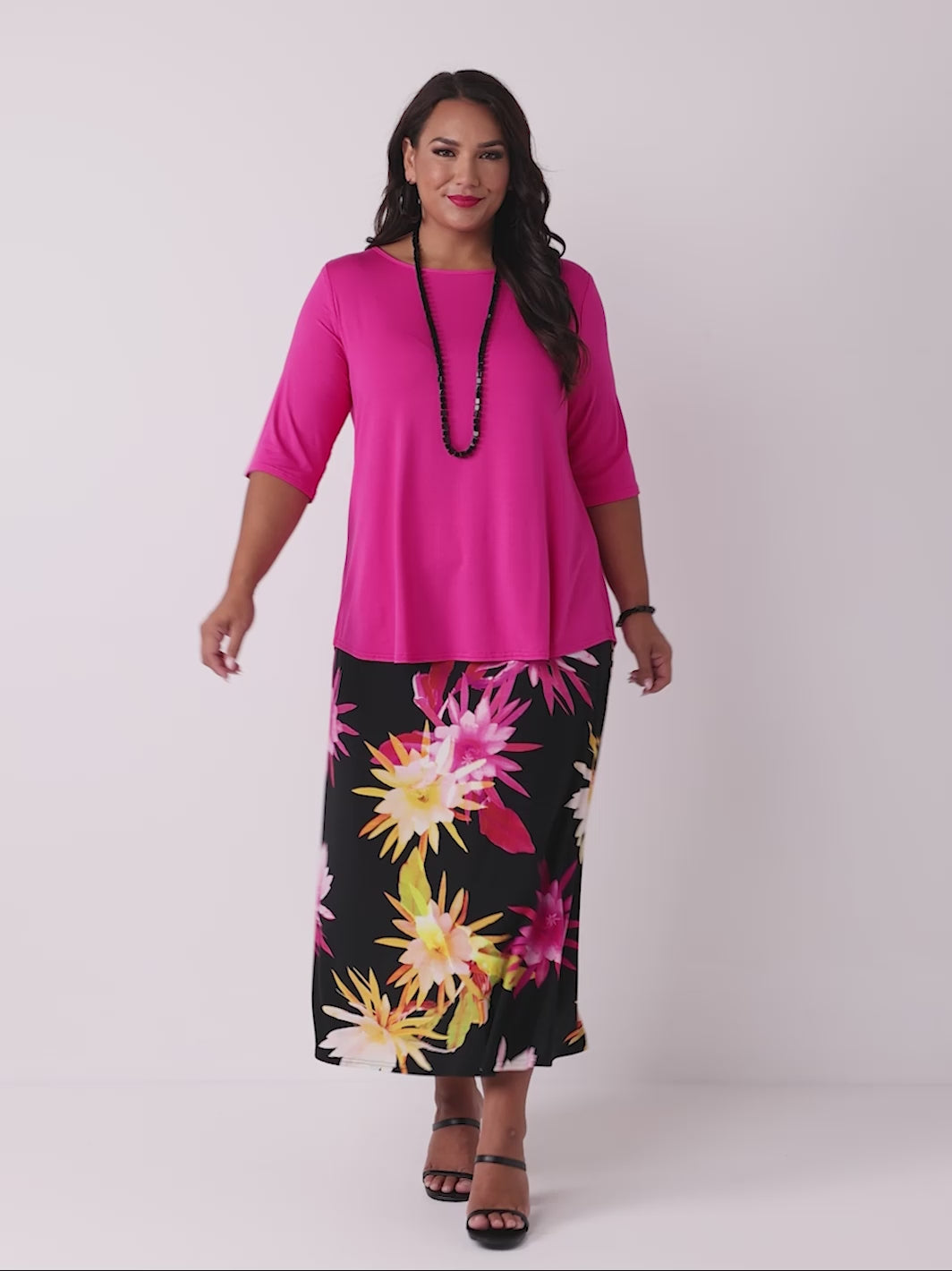 video of model wearing a pink basic tee styled with a black midi skirt with a vibrant, large-scale tropical floral print in pink and yellow
