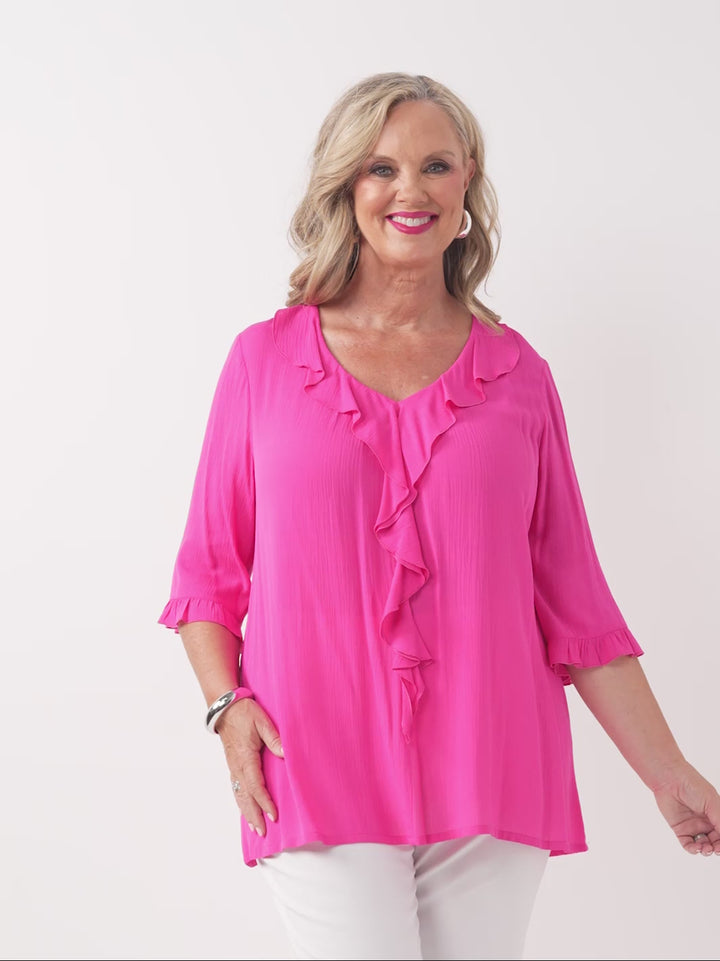 video of model wearing a bright pink ruffled blouse with three-quarter sleeves and white pants