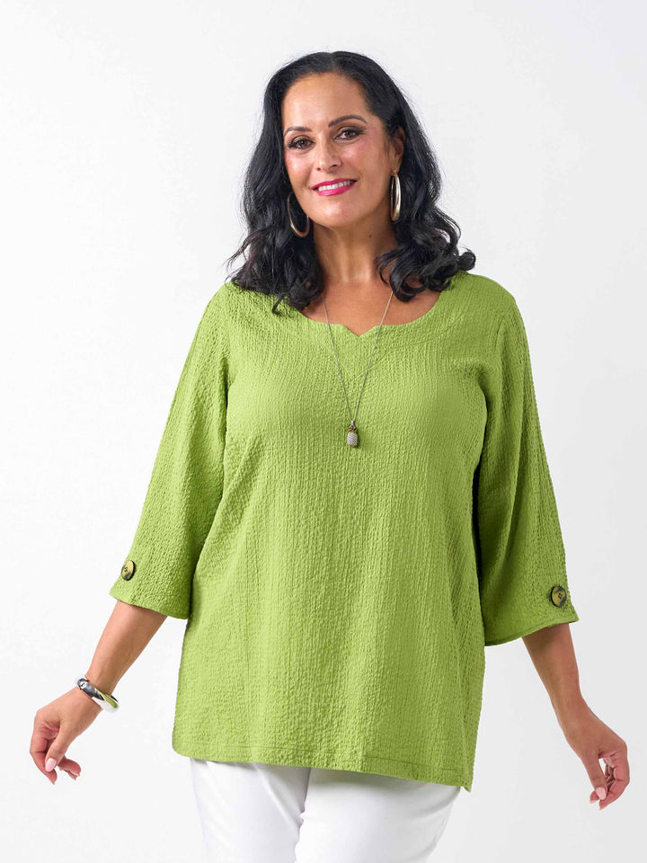 video of model wearing a lime green textured three-quarter sleeve top with decorative buttons on the cuffs