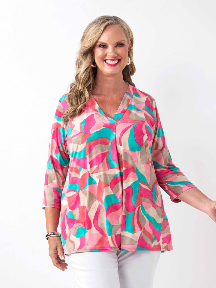 A woman wearing a colourful abstract print top in pink, with three-quarter sleeves and white pants