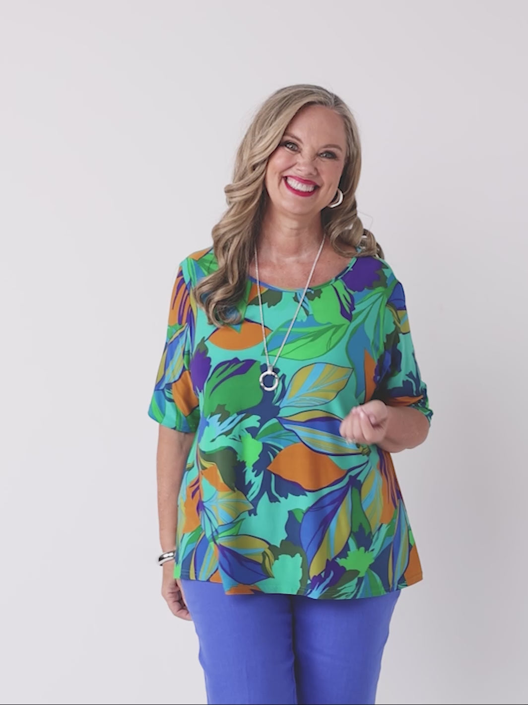 video of model wearing a short-sleeve top with a bold tropical leaf print in green, blue, and orange